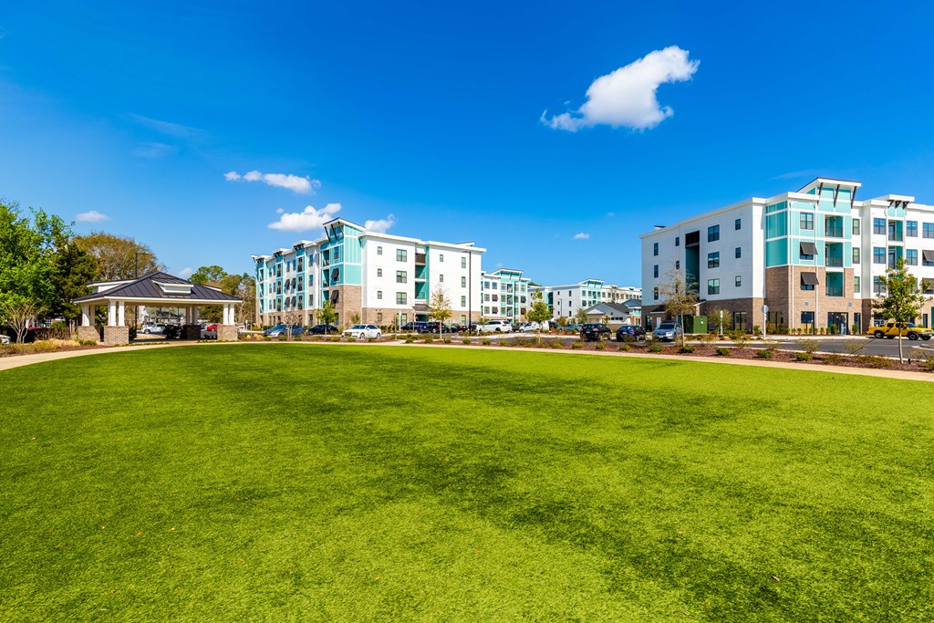 a large grassy field with apartment buildings in the background