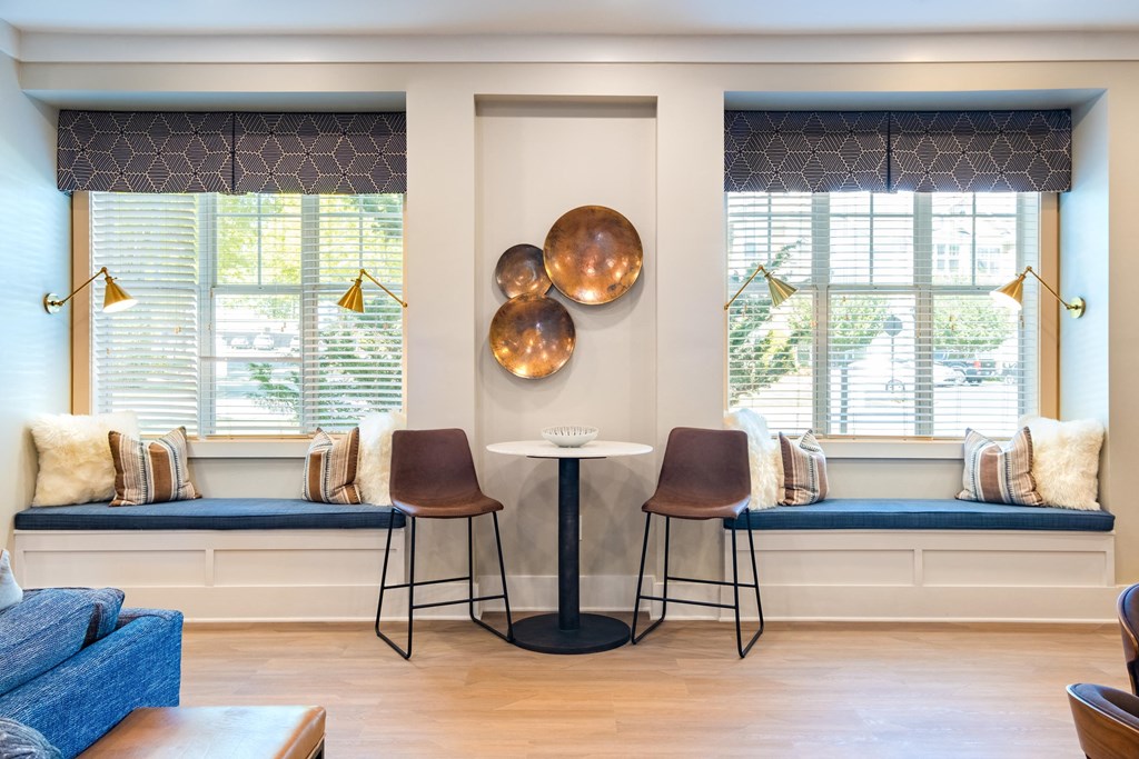 a seating area with two windows and two stools and a table