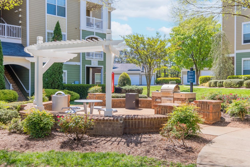a patio with a fire pit and a pergola in front of an apartment building