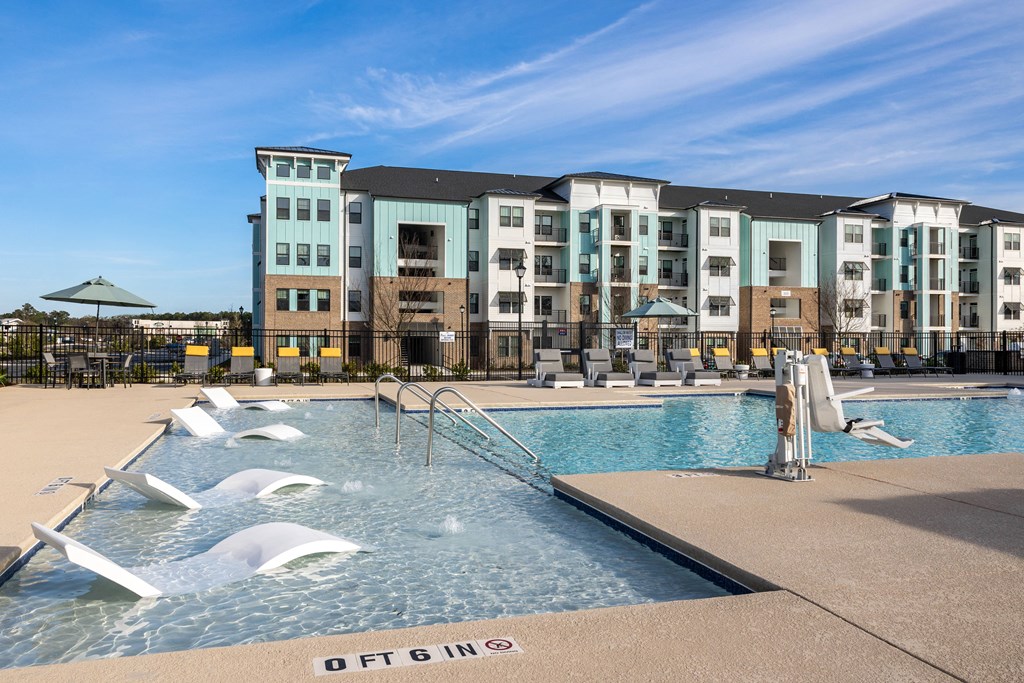 a swimming pool with chairs in front of an apartment building