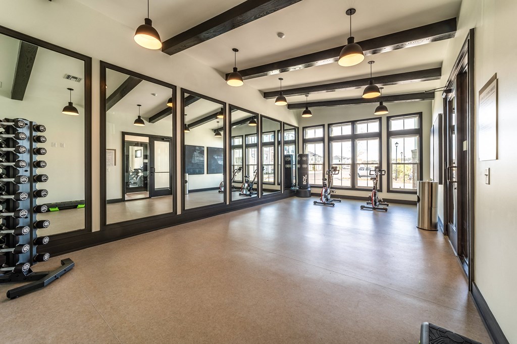 a gym with mirrors and weights on the floor and a row of windows