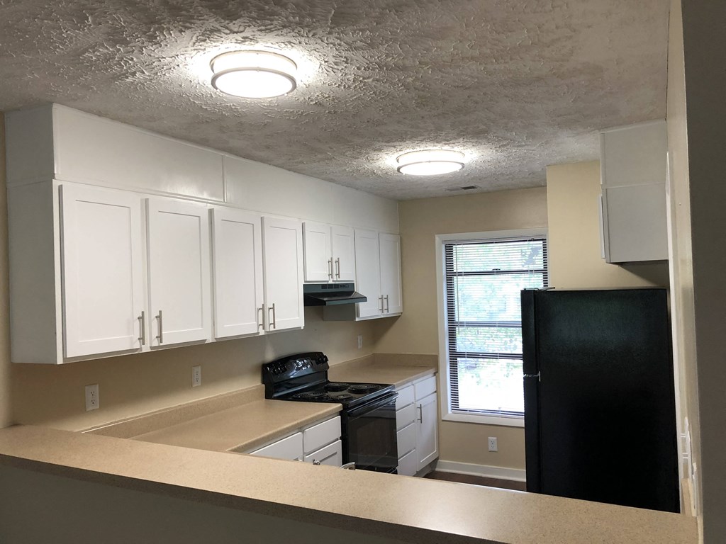 an empty kitchen with white cabinets and a black refrigerator