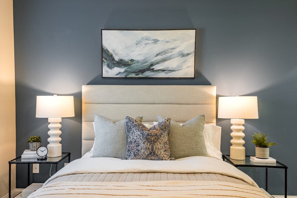 a bedroom with a bed and two lamps and a painting on the wall