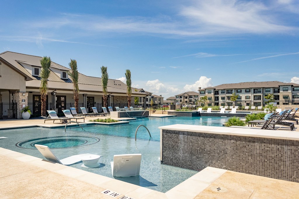 a large swimming pool with lounge chairs and buildings in the background
