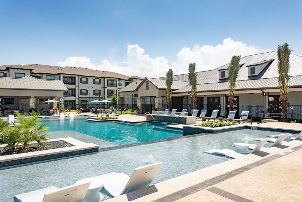 a large swimming pool with lounge chairs and buildings in the background