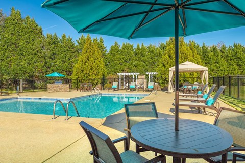 A poolside table with chairs and an umbrella overlooking a pool.