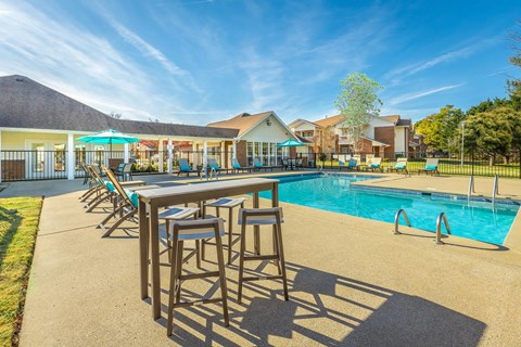 A poolside bar area with a row of stools and a table.