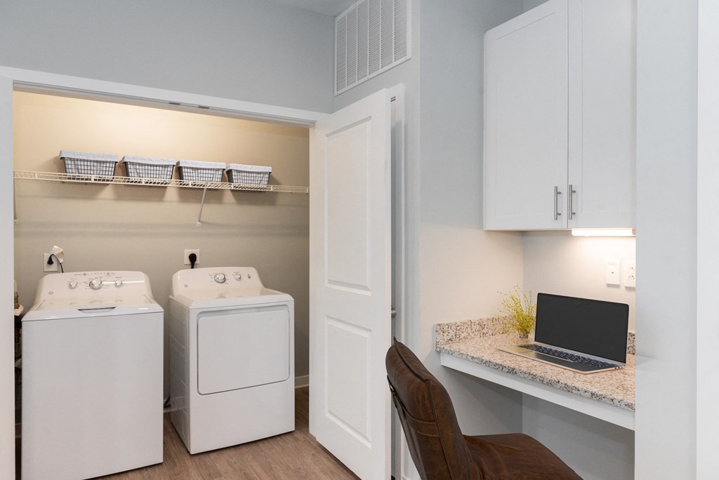 a desk with a laptop and a washer and dryer in a laundry room