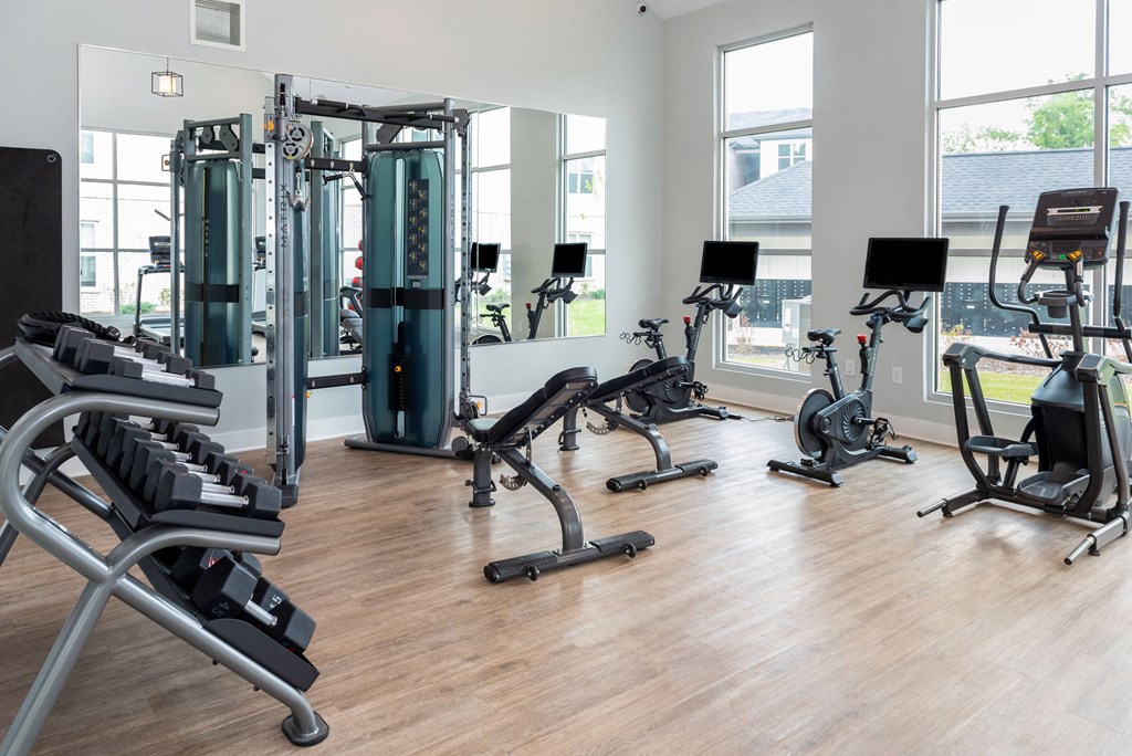 a fitness room with weights and cardio equipment and windows