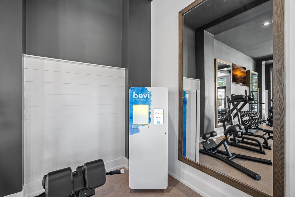 A gym with a mirror reflecting a treadmill and weights and Bevi Station.