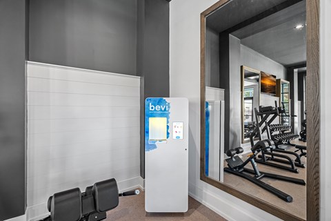 A gym with a mirror reflecting a treadmill and weights and Bevi Station.