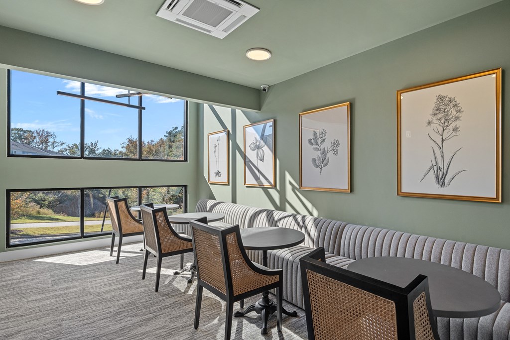 A room with a seating bench, round tables and chairs, and a window with a view of trees.