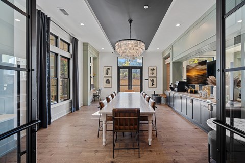 Clubhouse with a long table, multiple chairs and a chandelier hanging from the ceiling.