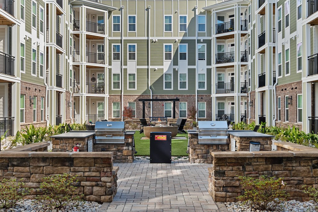 A courtyard surrounded by buildings with a stone wall and grills in the center.