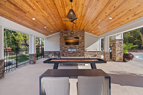 Outdoor patio with a stone fireplace and a wooden ceiling with seating and games.