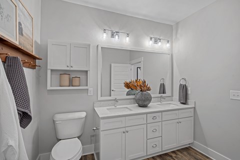 A white bathroom with a double sink, mirror and toilet.