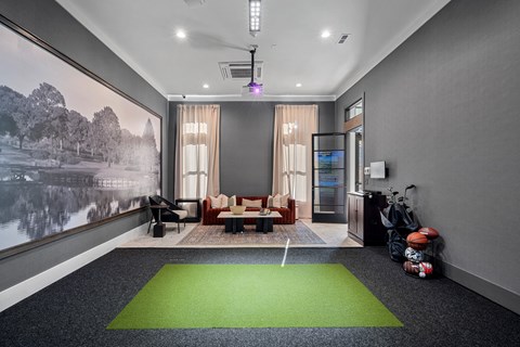 A room with golf simulator, putting green on the floor and a couch for seating.