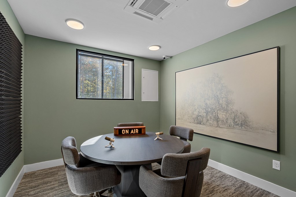A conference room with a round table and chairs plus a large picture on the wall.
