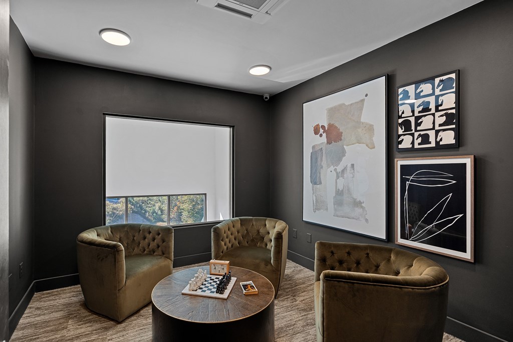 A dark colored room with a coffee table, chairs and pictures on the wall.