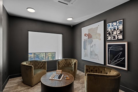 A dark colored room with a coffee table, chairs and pictures on the wall.