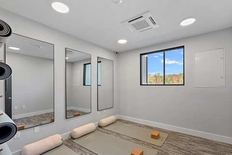 A spacious fitness studio room with a large mirror and a window showing a blue sky.