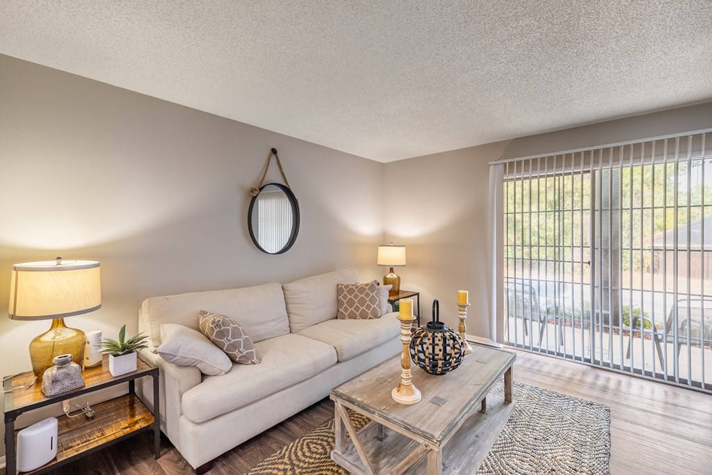 A well-lit living room with a white couch, a glass coffee table, and a yellow lamp.