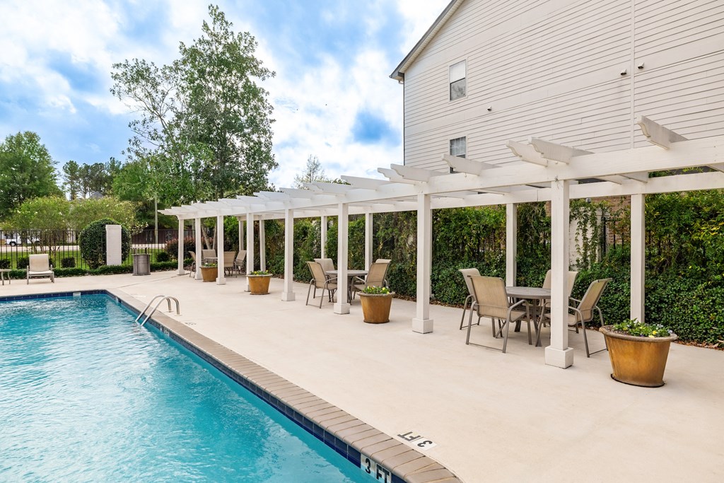 A pool with a white pergola and chairs around it.