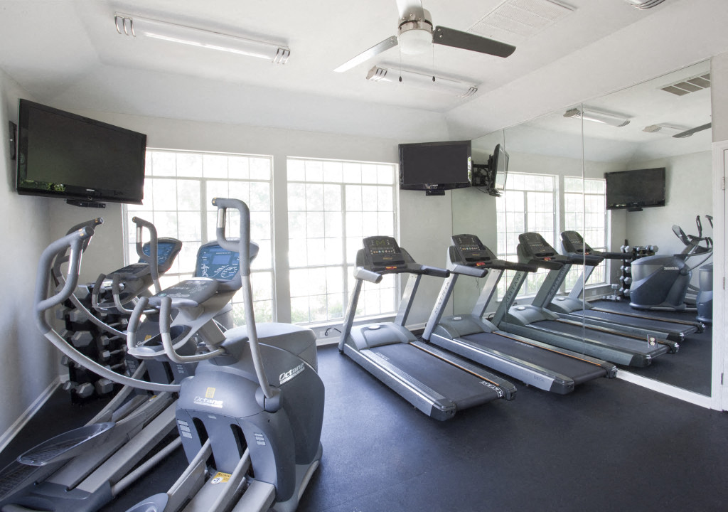 a gym with cardio equipment and tv on the wall