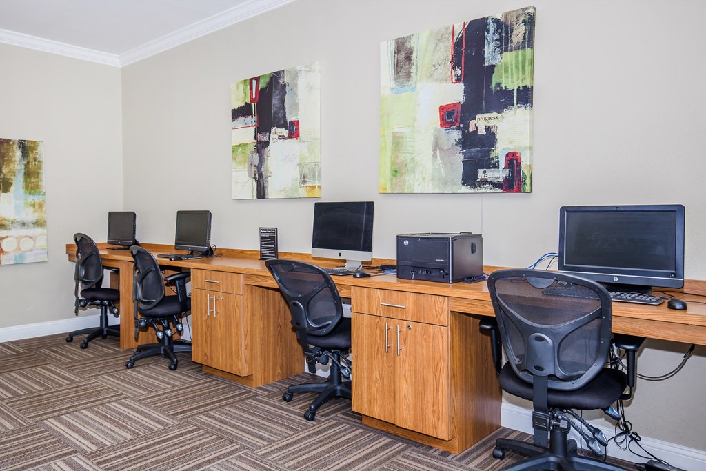 two desks with computers and chairs in a room with paintings