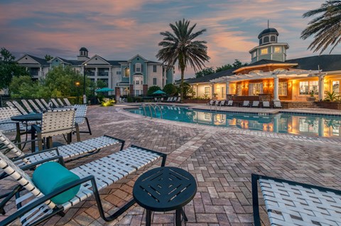 A poolside area with lounge chairs and a table in front of a building with a tower.