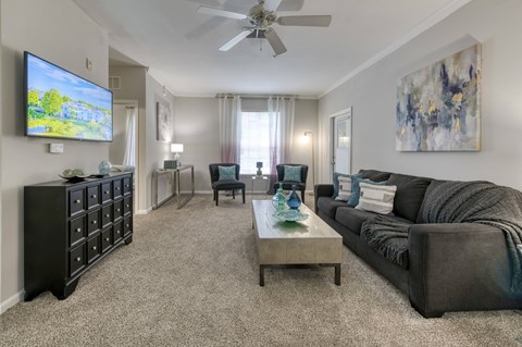 A living room with a grey couch, a black cabinet, a coffee table, and a television on the wall.