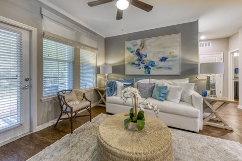 A living room with a white couch, a table with a vase of flowers, and a painting on the wall.