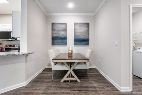 A dining room with a table and chairs and a painting on the wall.