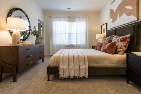 A bedroom with a bed, nightstand, and a dresser with a lamp on it.