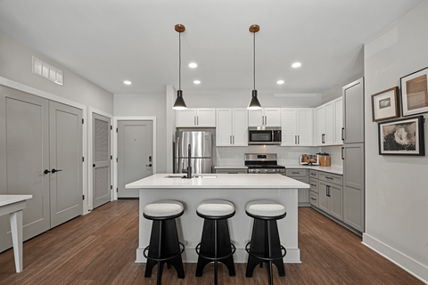 A modern kitchen with a white island and black bar stools.