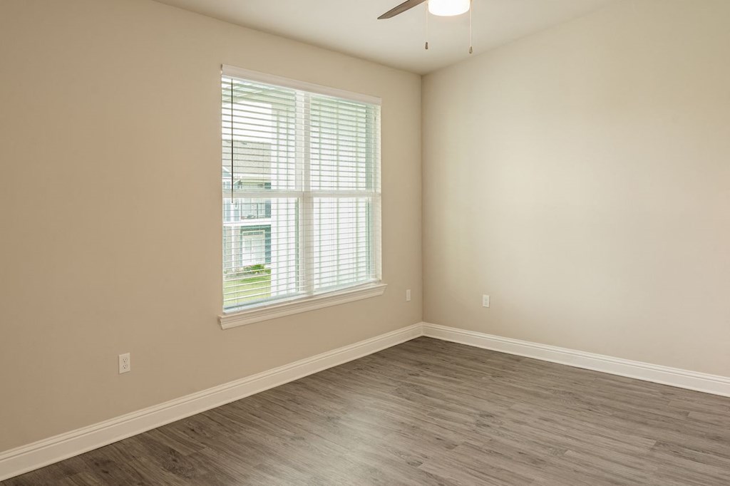 an empty bedroom with a large window and hardwood floors