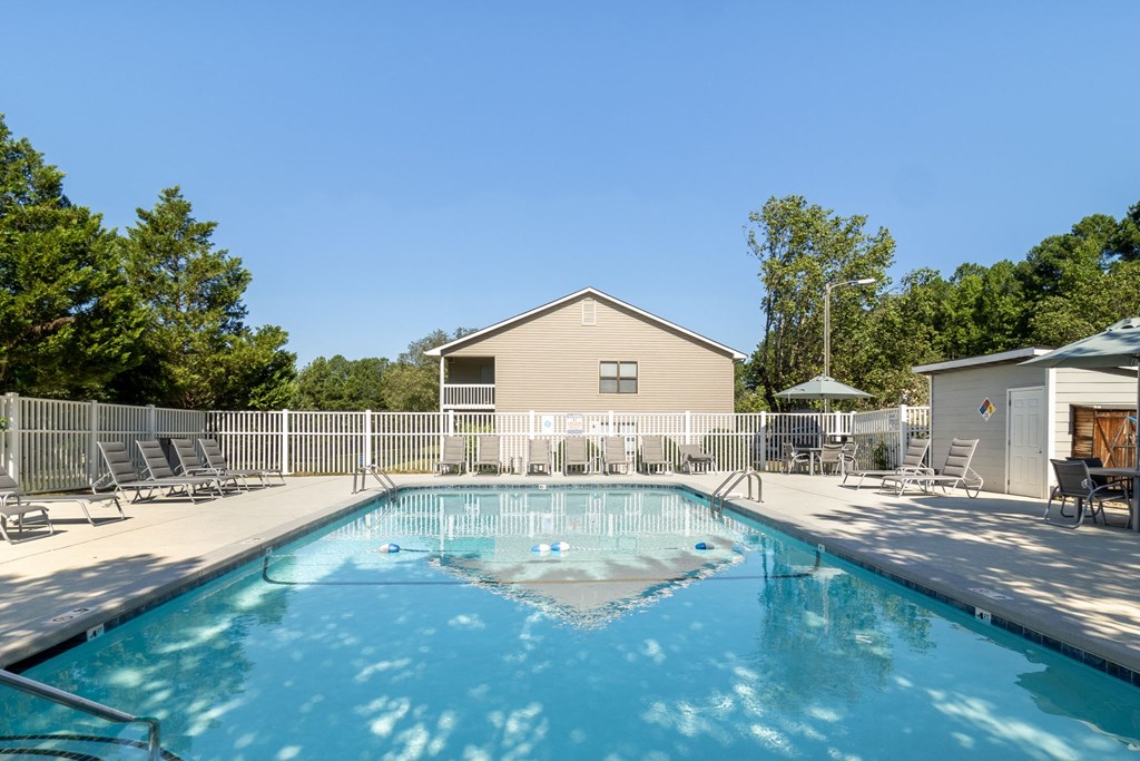 our resort style swimming pool is next to our house with chairs and a fence
