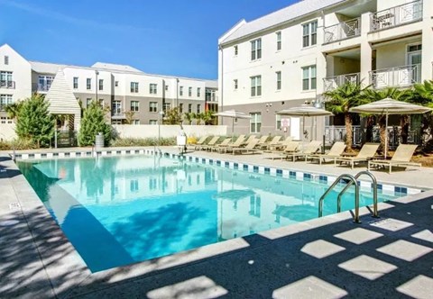Outdoor swimming pool with loungers and umbrellas and exterior building in the background.