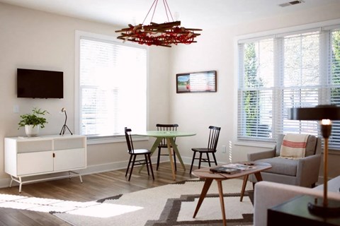 A living room with a white cabinet, a black TV, a wooden table and chairs, and a red chandelier.