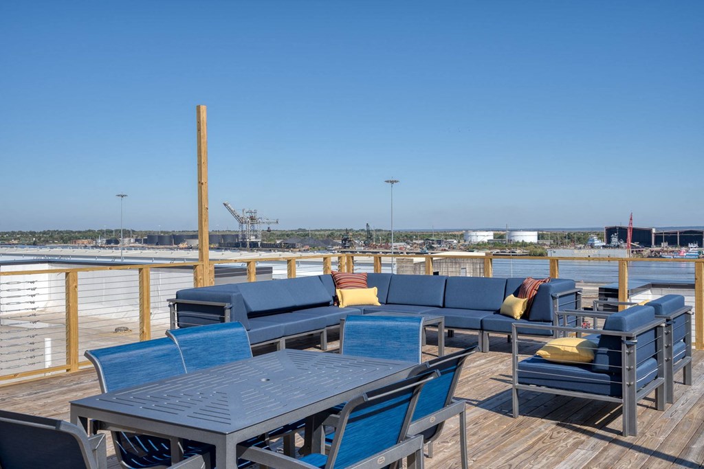 a deck with blue couches and tables and chairs overlooking the water