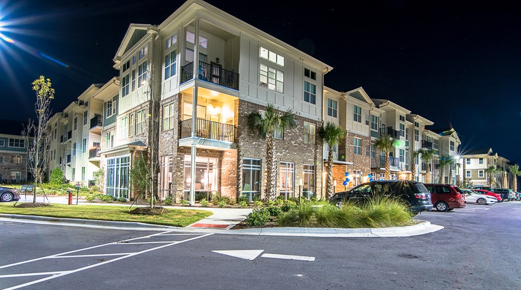 a row of apartment buildings at night with a parking lot in the foreground
