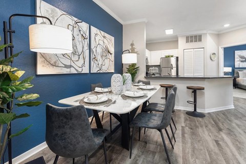 A dining room with a table set for two and a kitchen area in the background.