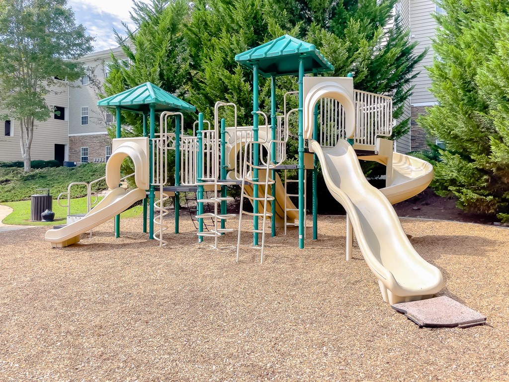 a playground with two slides and two umbrellas in a park