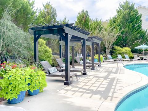 a poolside pergola with lounge chairs next to a pool