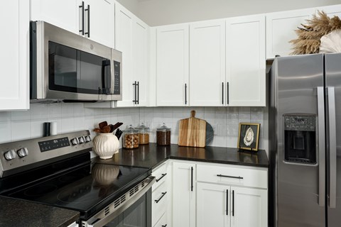 A kitchen with white cabinets and black countertops.