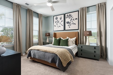 A bedroom with a large bed, a ceiling fan, and a painting on the wall.