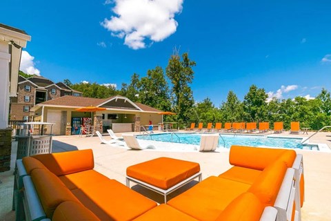 A pool area with orange sun loungers and a white building in the background.