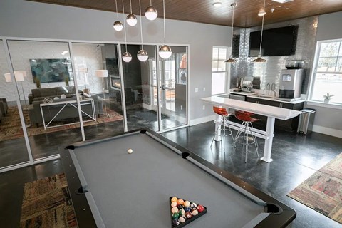 A pool table is in the middle of a room with a kitchen in the background.