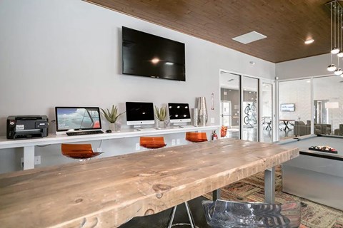 A long wooden table with computer stations and a TV mounted on the wall.