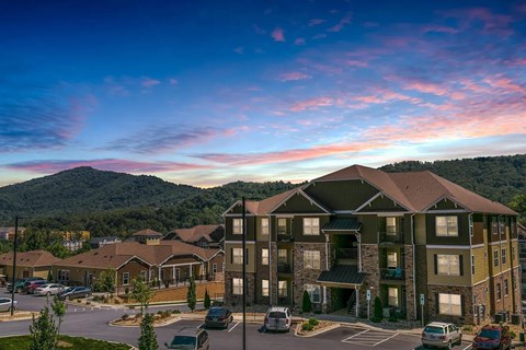 A large apartment complex with a parking lot in front and view of mountains behind.